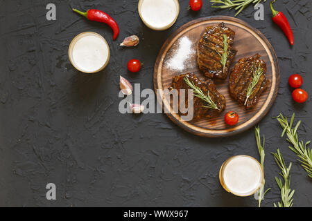 Des steaks délicieux barbecue et de la bière dans des verres sur une pierre noire, avec les tomates cerises et les enfants. Banque D'Images