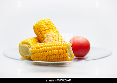 La vie encore d'épis de maïs et tomates sur une plaque de verre. Isolé sur fond blanc. Petite Profondeur de champ. Banque D'Images