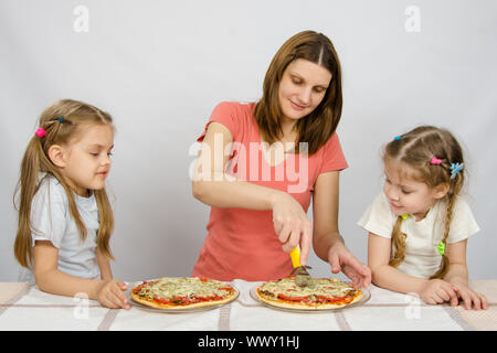 Maman coupe la pizza, et l'attendons avec deux petites filles Banque D'Images