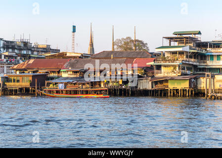 Bateau à longue queue en face de maisons sur pilotis le long de la rivière Chao Phraya à Bangkok Banque D'Images