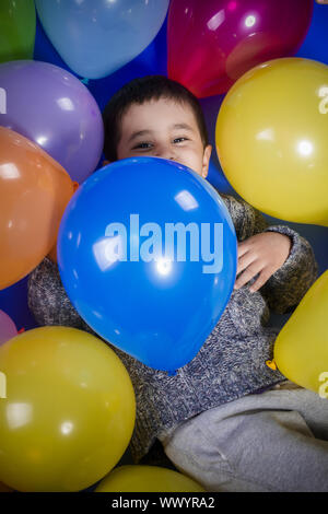 Fun, Brunette Garçon jouant avec beaucoup de ballons colorés, de sourires et de joie at Birthday party Banque D'Images