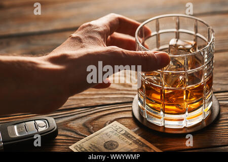 La main de l'homme atteindre au verre avec de l'alcool boire et clé de voiture. Boire et conduire concept. Banque D'Images