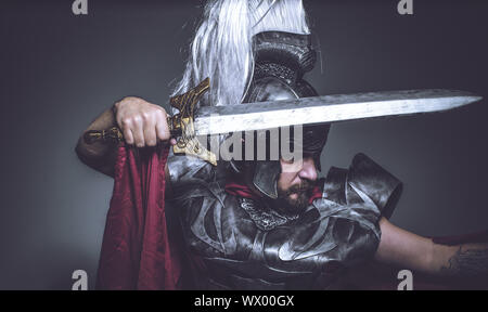 Lutteur, gladiateur romain et guerrier de Rome avec casque et manteau rouge, porte une épée de fer, barbe et cheveux longs. Banque D'Images