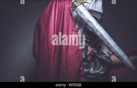 Lutteur, gladiateur romain et guerrier de Rome avec casque et manteau rouge, porte une épée de fer, barbe et cheveux longs. Banque D'Images