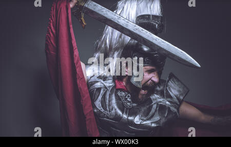 Lutteur, gladiateur romain et guerrier de Rome avec casque et manteau rouge, porte une épée de fer, barbe et cheveux longs. Banque D'Images