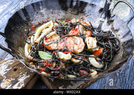 Linguine italienne con tinta de calamars et crevettes roses avec des olives en gros plan sur une grande colère poêle de fer
