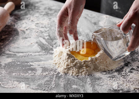 Women's Hands verse de l'eau dans la farine sur la table de la cuisine. Préparation de la pâte à cuire Banque D'Images