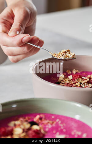 A woman's hand est titulaire d'une cuillère de gruau sur une plaque avec des smoothies. Un petit-déjeuner sain Banque D'Images