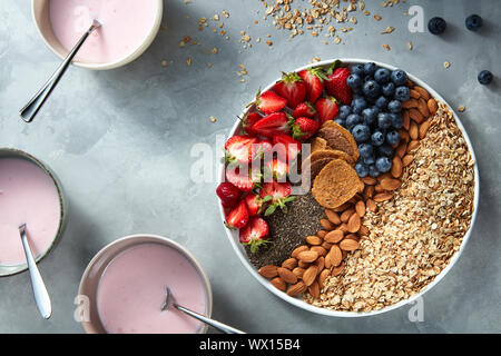 Le yogourt dans des verres avec le muesli, fruits et graines de chia pour petit-déjeuner sain sur un fond en béton Banque D'Images