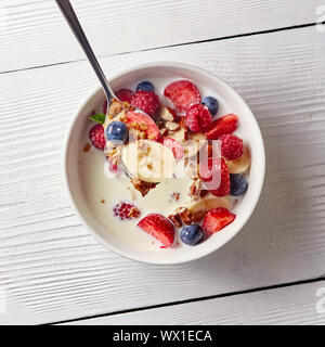 Ingrédients naturels tranches de banane, myrtille, fraise, granola dans la cuillère. Des produits naturels faits à l'alimentation dans le bo blanc céramique Banque D'Images