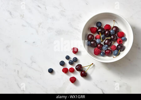 Bleuets frais bio, cerise, framboise dans un plat de céramique sur un fond noir en gris avec place pour le texte. Vue d'en haut. Banque D'Images