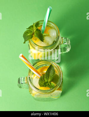 Les agrumes des tranches de citron et de lime, la glace, l'eau et des pailles en plastique dans le verre sur un fond vert. Deux pots en verre avec un Banque D'Images