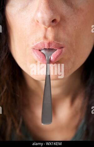 Femme adulte face avec une cuillère en métal dans sa bouche Banque D'Images