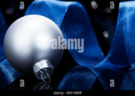 Bal de noël argent mat en face d'un ruban bleu sur noir fond réfléchissant Banque D'Images