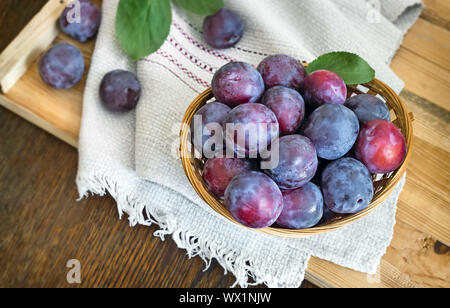 Les prunes mûres dans un grand panier en osier. Banque D'Images