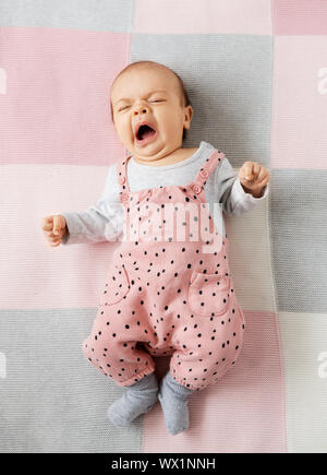 Yawning baby girl in pink suit lying on blanket Banque D'Images