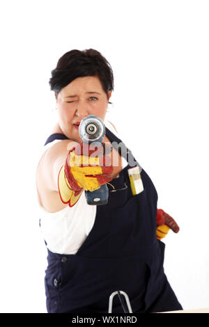 Femme espiègle en salopette et un tablier en tenant avec pour objectif une perceuse électrique de poche comme elle s'amuse pendant un projet de bricolage Banque D'Images