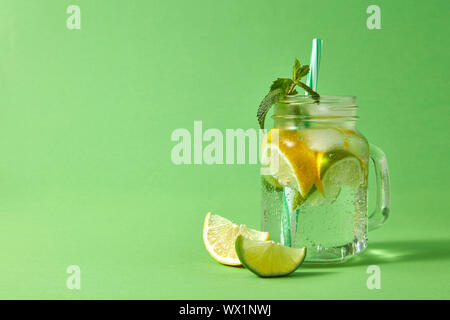 Pot Mason avec des limonade pétillante aux agrumes, des cubes de glace, feuille de menthe et de pailles en plastique sur un dos vert Banque D'Images