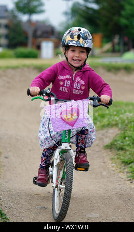 Une petite fille (5 ans) rayonnant de joie comme les manèges son vélo Banque D'Images