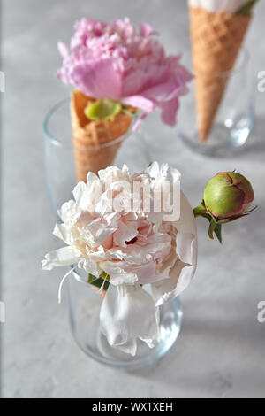 La floraison blanche et rose avec bud piones, feuille verte dans un verre, les cônes gaufrette sur un tableau gris. Banque D'Images