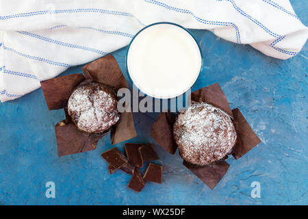 Deux muffins au chocolat, chocolat noir et un verre de lait sur un fond bleu. Vue d'en haut. Banque D'Images