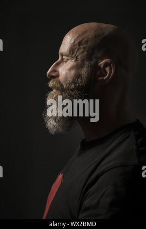 Un homme barbu aux yeux clos Vue de côté et un arrière-plan sombre Banque D'Images