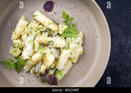 Style moderne allemande traditionnelle salade de pommes de terre et de l'asperge blanche et cornichon comme close up sur une plaque avec copie espace droit Banque D'Images