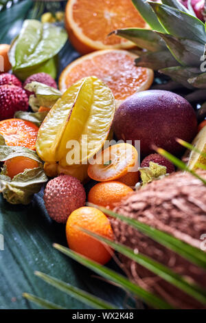 Fruits exotiques d'été - carambole, ananas, noix de coco, mangue, kiwi, les moitiés d'orange sur une feuille tropicale verte. Banque D'Images