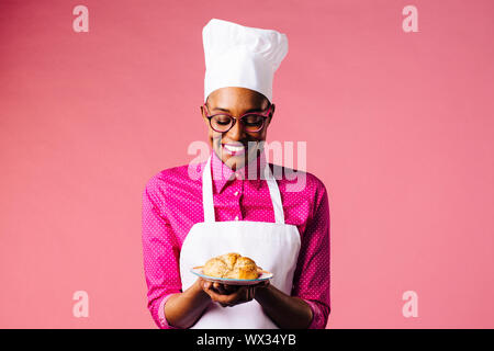 Portrait of a smiling young female chef holding a plate avec un croissant frais Banque D'Images