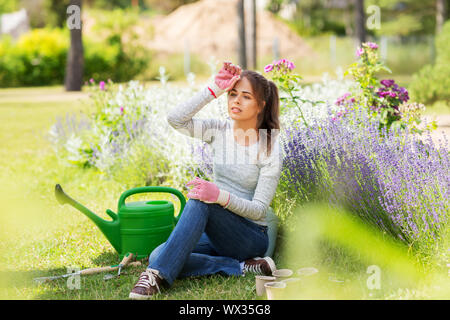 Jeune femme fatiguée avec outils de jardin en été Banque D'Images