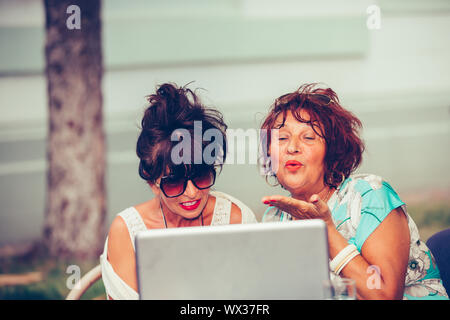 Deux femmes - happy friends sitting in a cafe envoyer un baiser en ligne pendant un appel vidéo avec un ordinateur portable. Banque D'Images