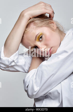 Portrait d'une jeune femme blonde en blouse blanche sur fond gris Banque D'Images