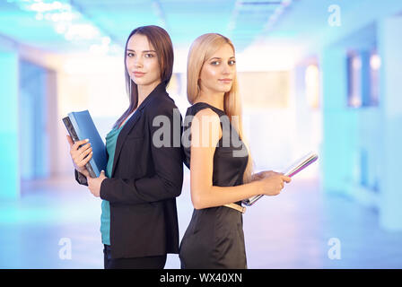 Deux filles dans le bureau avec les dossiers avec des documents en main. Les jeunes femmes de discuter des travaux de bureau. Banque D'Images