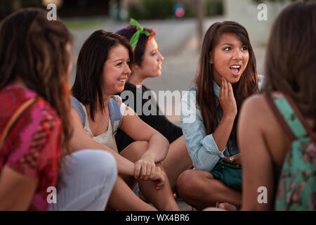 Dégoûté teenage girl sitting on le terrain en parlant avec des amis Banque D'Images