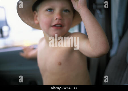 Un petit garçon souriant est perçu à l'intérieur d'une voiture portant un chapeau. Banque D'Images