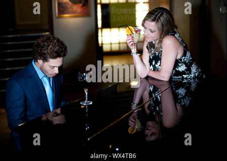 Woman enjoying cocktail et d'admirer l'homme joue du piano. Les jeunes adultes attrayant Banque D'Images