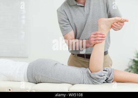 Femme couchée vers l'avant tandis que le physiothérapeute examinant sa jambe dans une chambre Banque D'Images