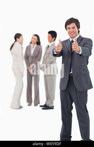 Vendeur giving Thumbs up avec des collègues derrière lui sur un fond blanc. Banque D'Images