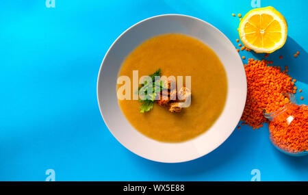 Lentilles soupe crème fraîche en plaque blanche sur fond bleu avec copie espace. Vue d'en haut. Le gruau de lentilles dans un bocal en verre et citron frais. Banque D'Images