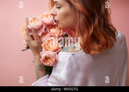 Une fille avec un tatouage est titulaire d'un bouquet de fleurs roses sur un fond pastel dans un quartier branché de l'année 2019 couleur corail vivant Pan Banque D'Images