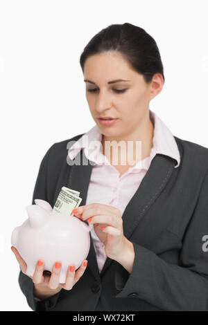 Brunette mettant l'argent dans un piggy-bank against white background Banque D'Images