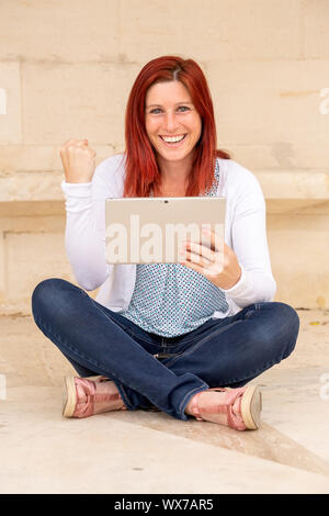 Portrait expressif d'un joli red-haired woman bonne lecture de l'information sur téléphone mobile Banque D'Images