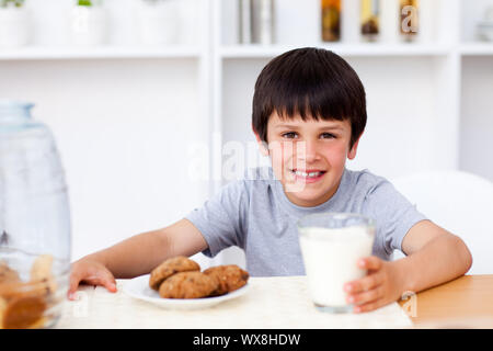 Happy boy manger des biscuits et boire du lait dans la cuisine Banque D'Images