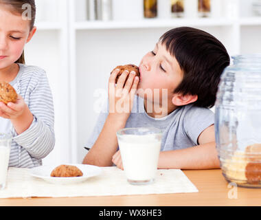 Sœur sourire manger des biscuits et boire du lait dans la cuisine Banque D'Images