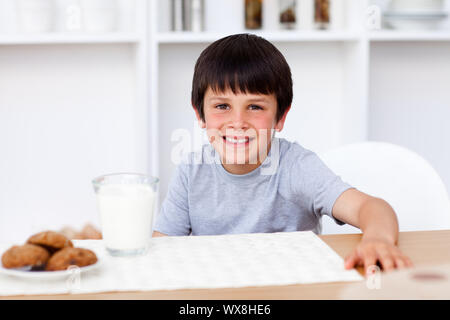 Smiling boy manger des biscuits et boire du lait dans la cuisine Banque D'Images