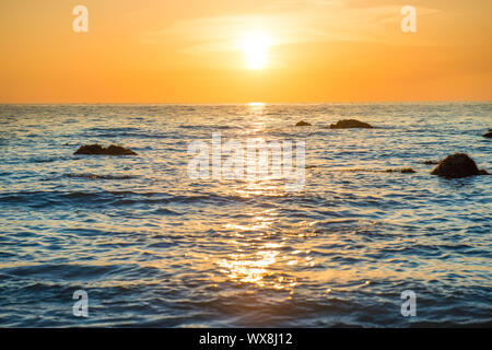 Paysage au coucher du soleil avec la plage, le soleil et des pierres sur mer Banque D'Images