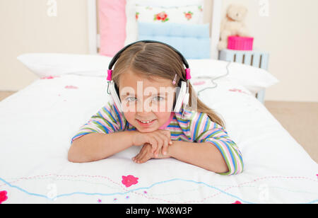 Cute little gril d'écouter de la musique allongée sur son lit Banque D'Images