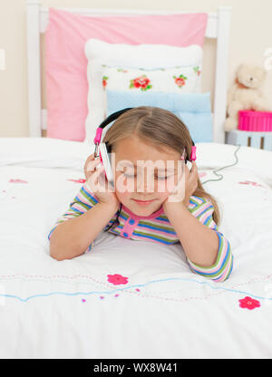 Beau petit gril à écouter de la musique avec des écouteurs lying on her bed Banque D'Images