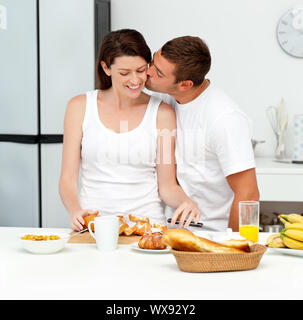 Homme passionné baiser sa petite amie tout en coupant le pain pour le petit-déjeuner dans la cuisine Banque D'Images