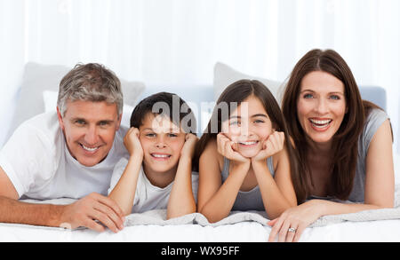 Famille heureuse regardant la caméra sur leur lit Banque D'Images